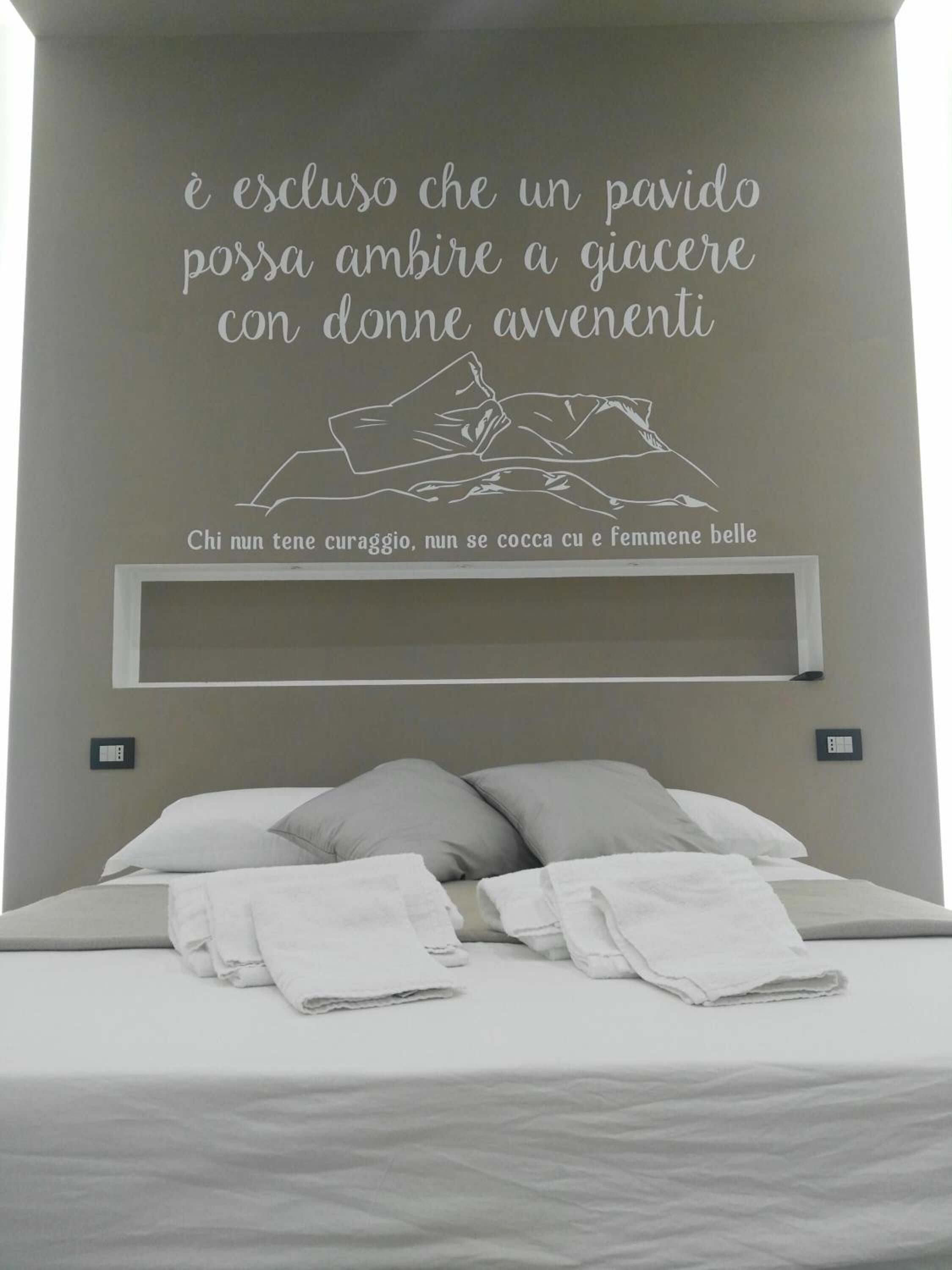 A bedroom with a bed, pillows, and a wall with text in Italian.