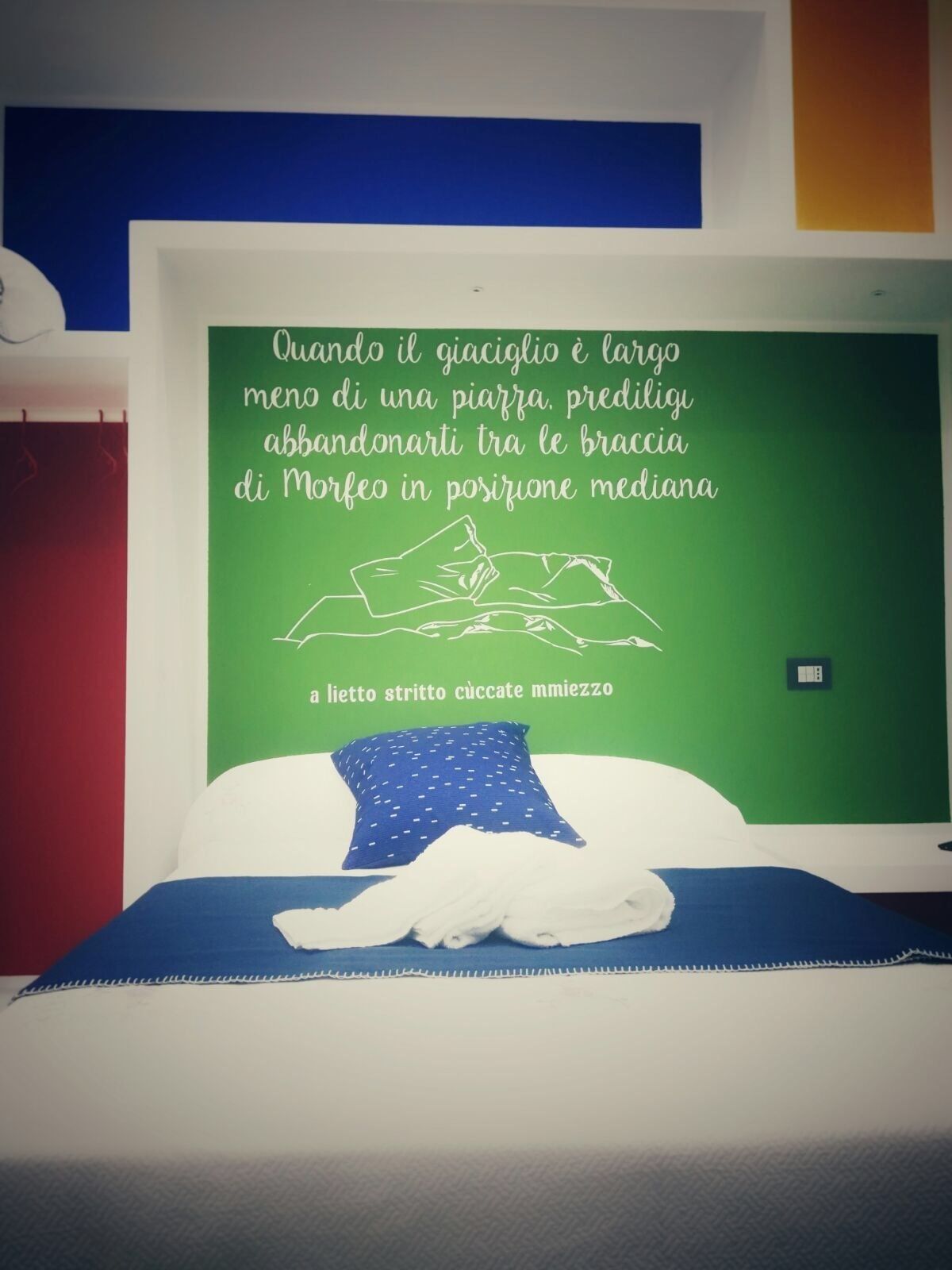 A bed with a green wall behind it, featuring a quote in Italian.