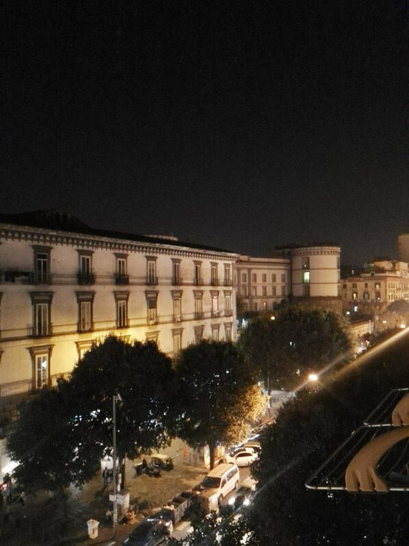A nighttime view of a building with multiple windows and balconies, surrounded by trees and parked cars. - B&B Next Stop Napoli (Naples)
