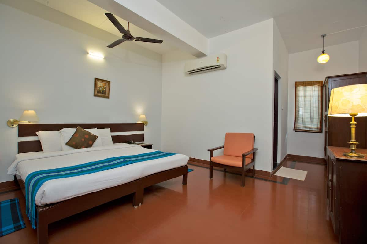 A hotel room with a bed, a chair, a desk, a ceiling fan, an air conditioner, and a window with curtains.