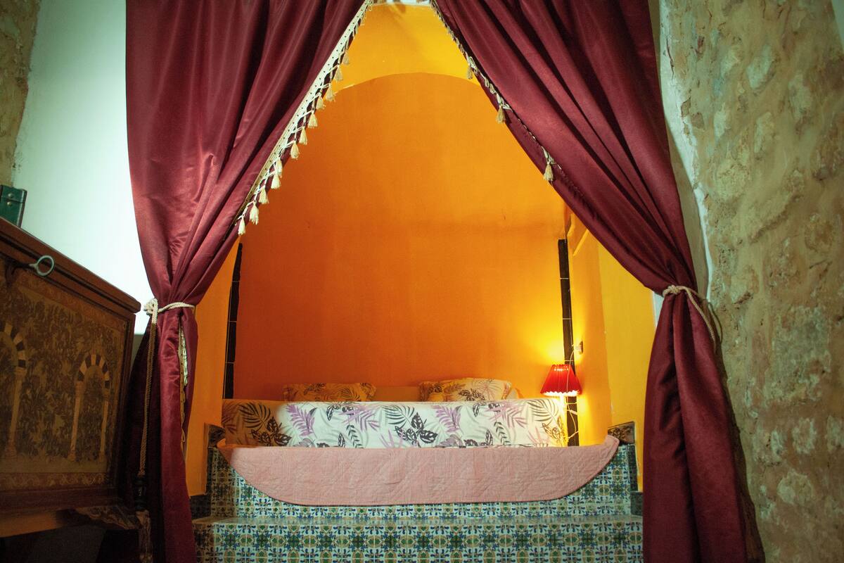 A room with a bed, draped curtains, and a patterned headboard.