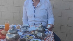 A person seated at a table with various dishes and a teapot, under a blue canopy, with a building and tower in the background. - Dar Kenza Tunis (Tunis)