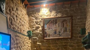 A cozy room with a stone wall, a bed with orange pillows, a TV, and a painting of a street scene. - Dar Kenza Tunis (Tunis)