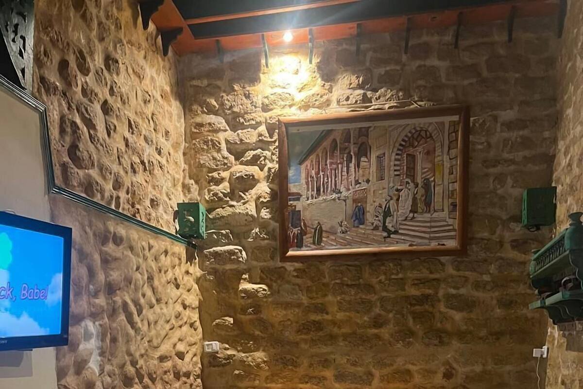 A cozy room with a stone wall, a bed with orange pillows, a TV, and a painting of a street scene.