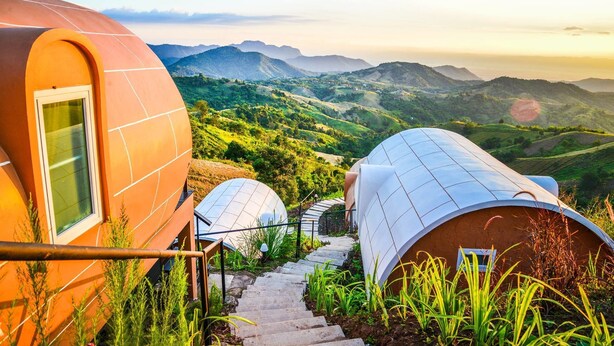 A modern, dome-shaped building with a staircase leading to a window, surrounded by lush greenery and mountains in the background. - Phu Sandao Resort (Khao Kho)