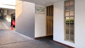 A hotel entrance with a sign reading 'WOW HOSTEL,' a red vehicle parked outside, and a staircase leading to an upper level. - Subwow Hostel (Bandung)