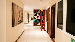 A hotel corridor with a tiled floor, a red chair, a geometric wall decoration, and a door with a sign. - Subwow Hostel (Bandung)