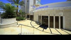 A modern building with a sign reading "La Palmorate." It features a central staircase, a covered outdoor area, and palm trees. - La Palmora Suites (Eilat)