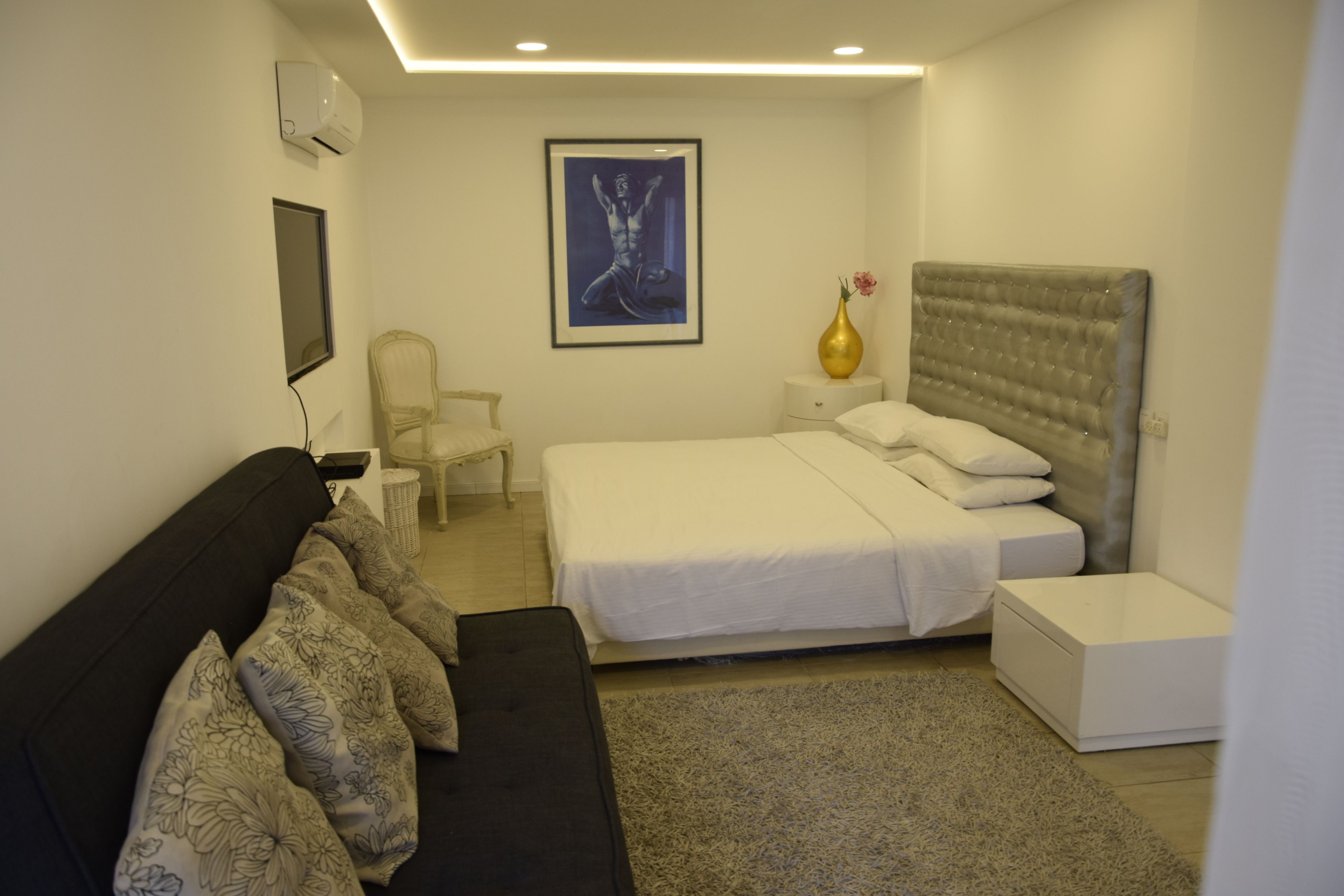 Une chambre moderne comprenant un lit, un canapé, un fauteuil, une table de chevet et une œuvre d’art encadrée accrochée au mur.