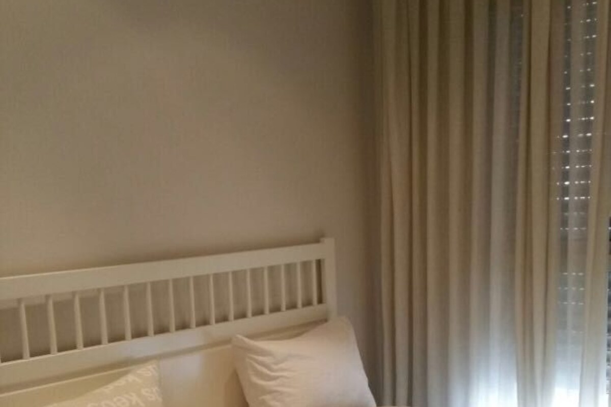 A neatly made bed with a patterned bedspread, a white headboard, and a bedside table with a drawer.