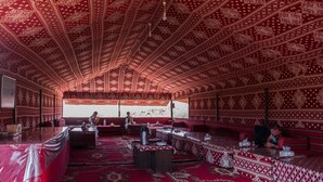 A traditional room with patterned red and white walls and ceiling, furnished with tables and benches, and a view of a mountainous landscape.