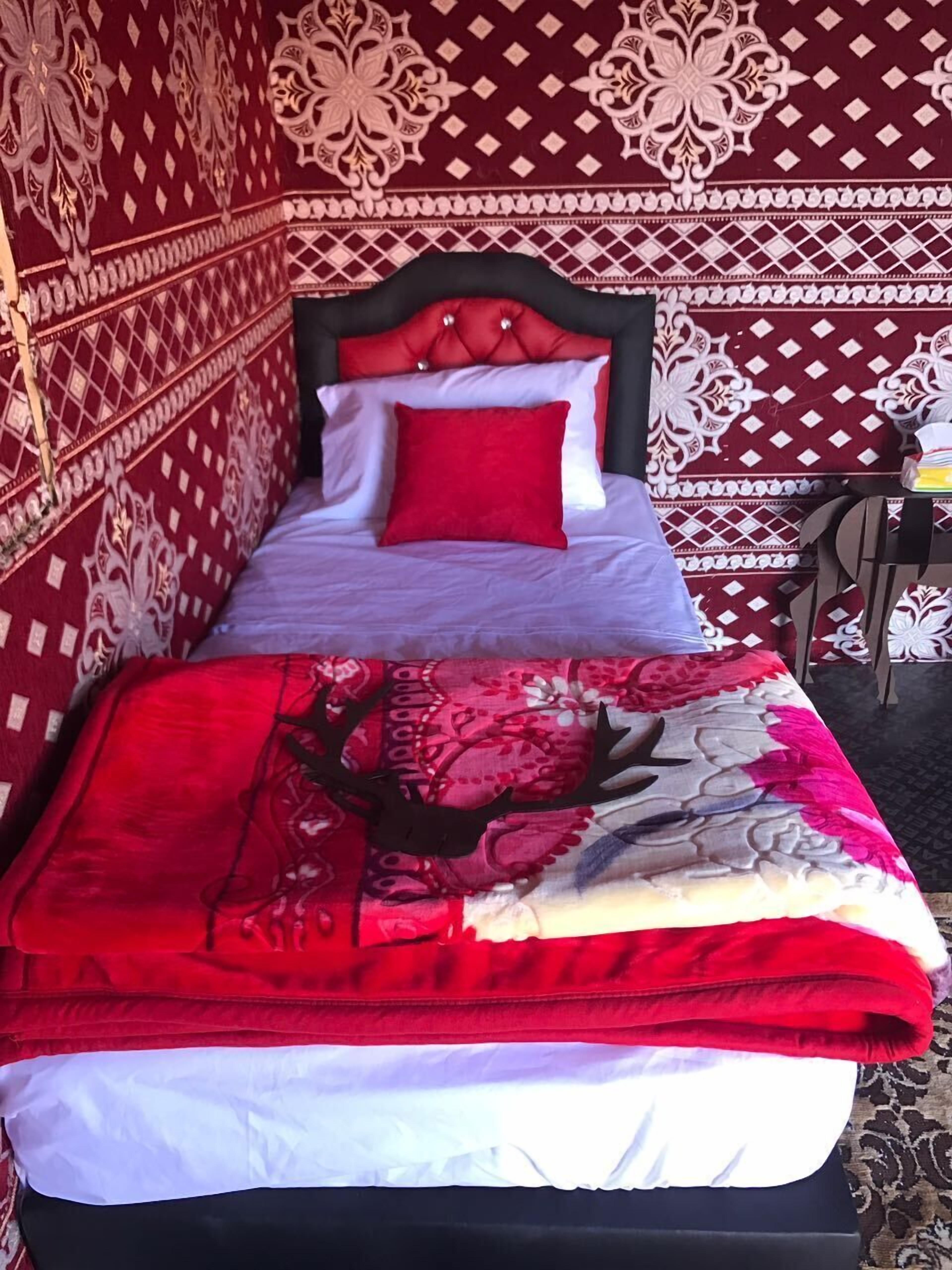 A bed with a red and white patterned bedspread, a red pillow, and a headboard with a decorative design.