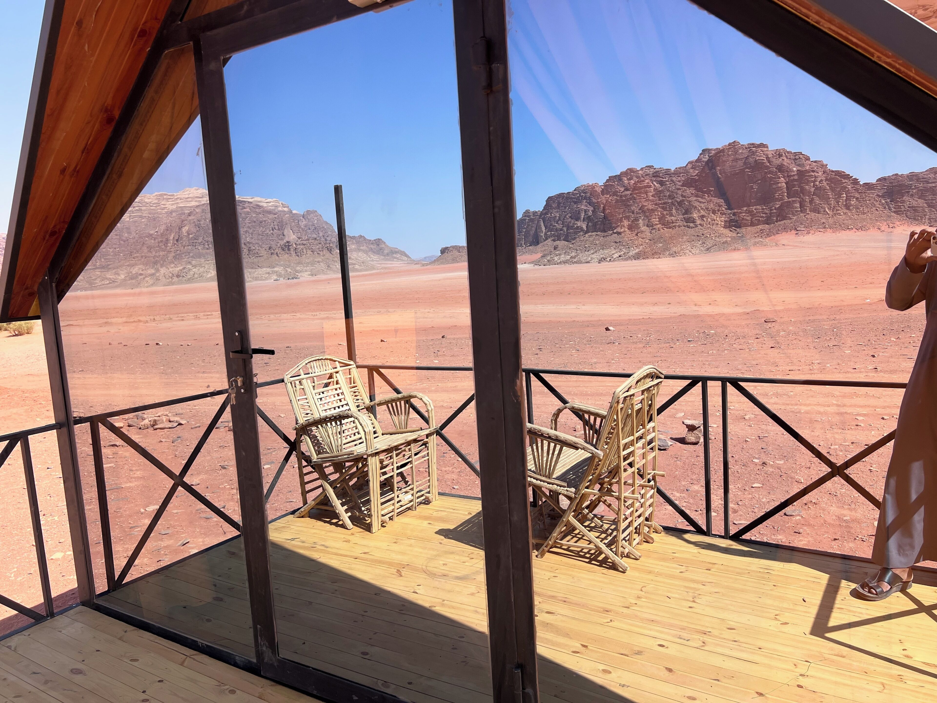 A wooden deck with wicker chairs, a view of a desert landscape with rock formations, and a clear sky.