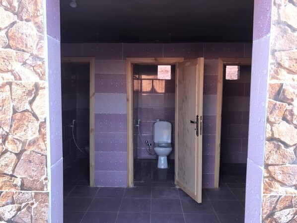 A bathroom with a toilet, shower, and a stone wall. - Wadirum Quiet Village Camp (Wadi Rum)