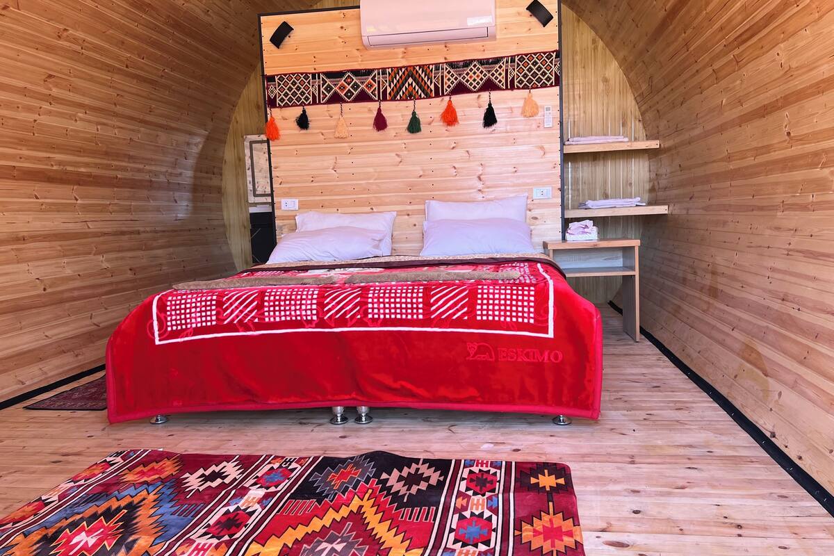 A cozy, wooden-paneled room with a bed, a red blanket, and a patterned rug.
