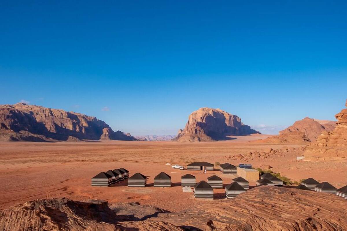 A desert landscape with rock formations and a row of tents.