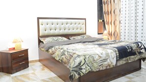 Un lit bien fait, recouvert d’une couvre-lit à motifs, une table de chevet en bois avec des tiroirs et une lampe.