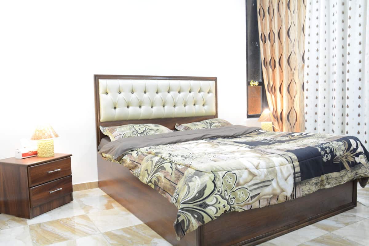 A neatly made bed with a patterned bedspread, a wooden nightstand with drawers, and a lamp.