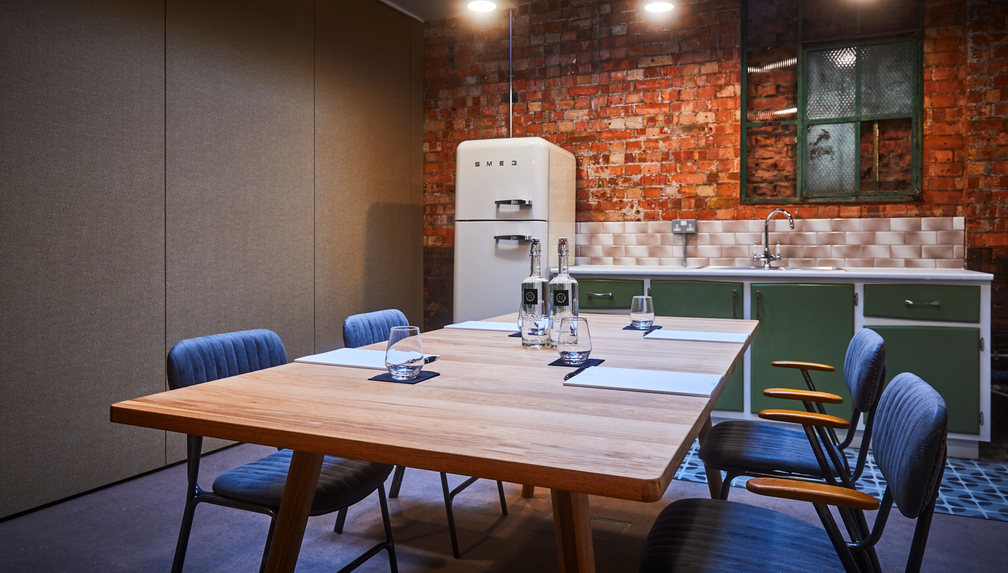 A modern kitchen with a brick wall, a white refrigerator, and green cabinets.