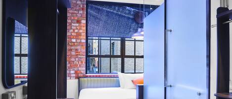 A modern hotel room with a brick wall, large windows, a bed, and a desk.