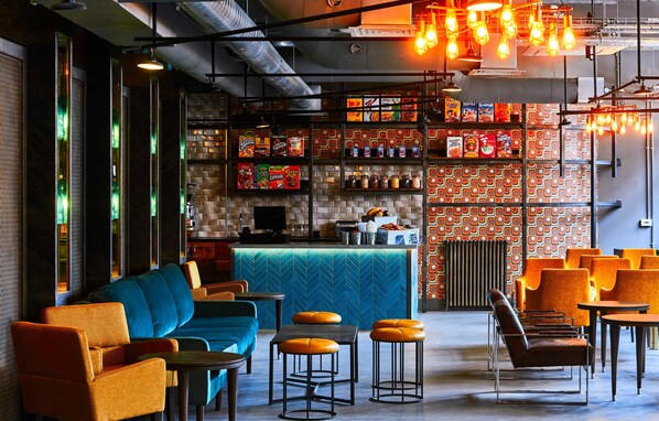 A modern bar area with seating, shelves of snacks, and a bar counter. - New Road Hotel (London)