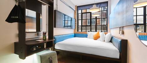 Una habitación de hotel moderna con una cama grande, un banco integrado, un espejo y vistas de la ciudad a través de amplias ventanas.