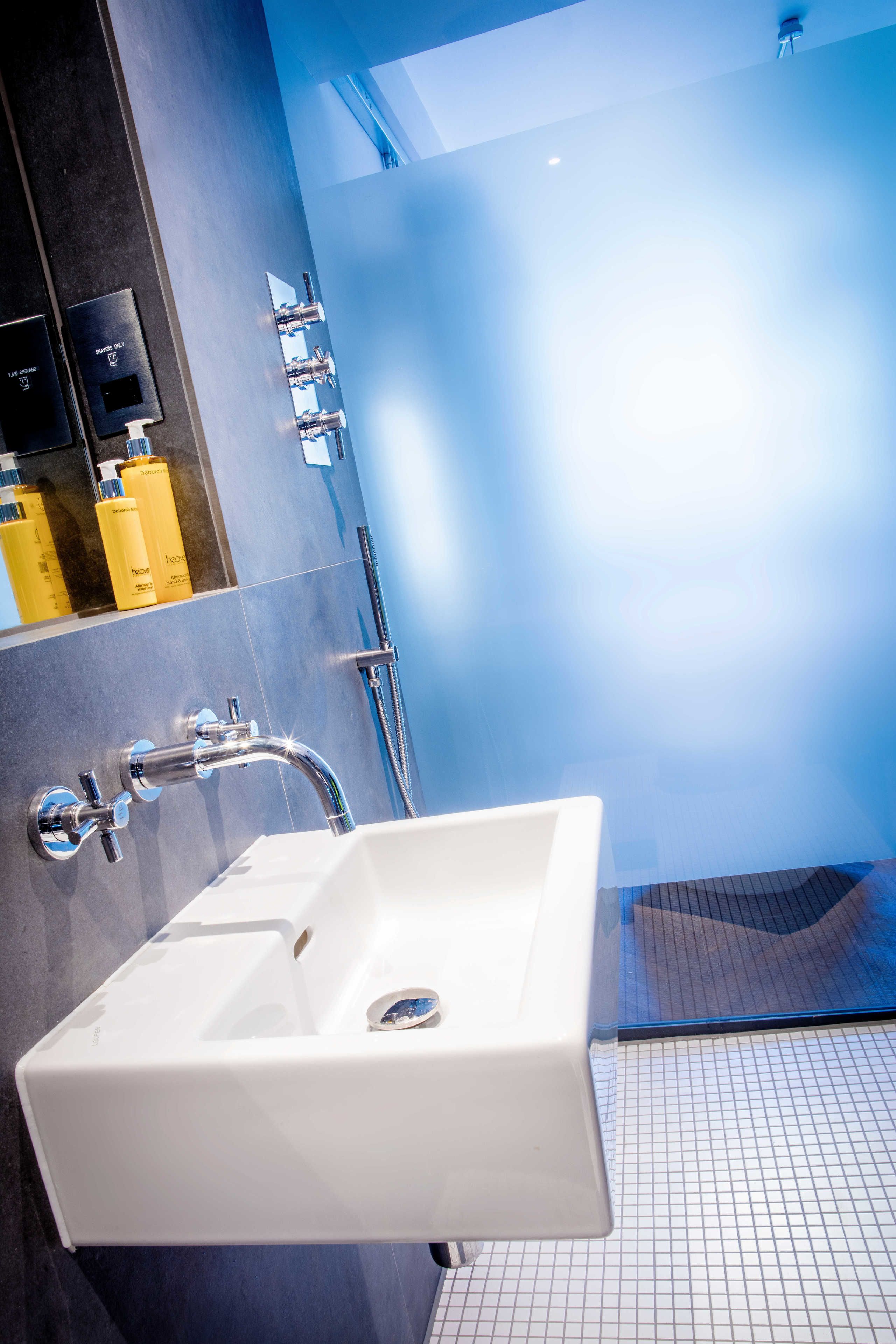 A modern bathroom with a white sink, chrome fixtures, and a blue-tiled wall.