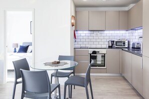 Uma cozinha moderna com uma mesa de jantar de vidro, cadeiras cinzentas e um micro-ondas.