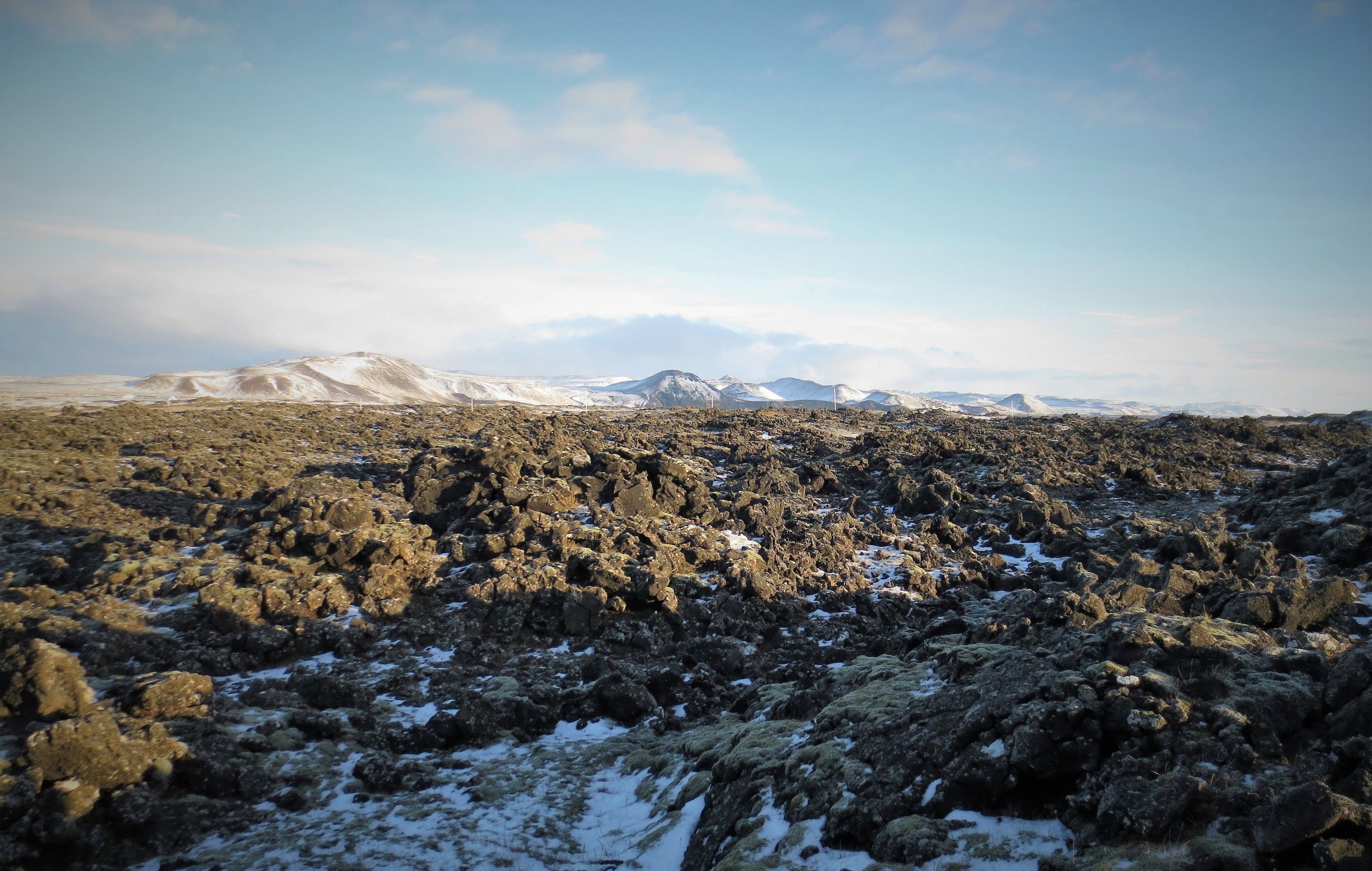 A rocky landscape with snow patches and distant mountains.