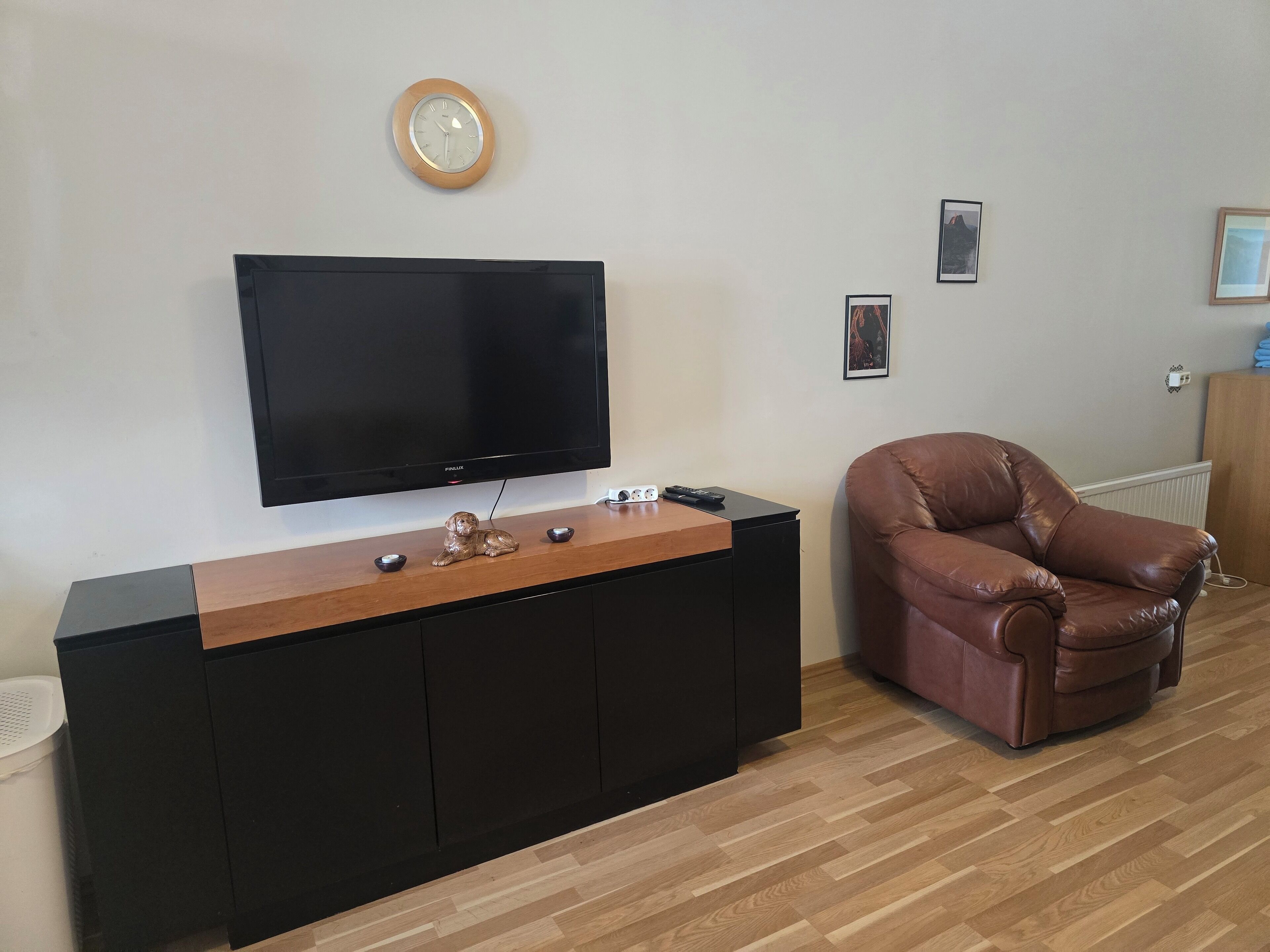 Un salon avec un téléviseur à écran plat fixé à un meuble de rangement noir, un canapé en cuir marron et une table basse en bois.