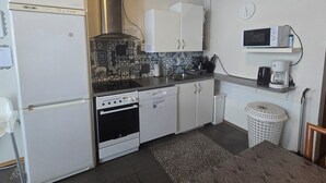 A compact kitchen with a refrigerator, stove, microwave, and coffee maker. - Reykjanes Guesthouse (Grindavik)