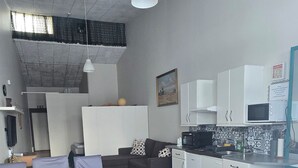 A compact kitchen with white cabinets, a microwave, and a sink. There is a dining area with a table and chairs. - Reykjanes Guesthouse (Grindavik)