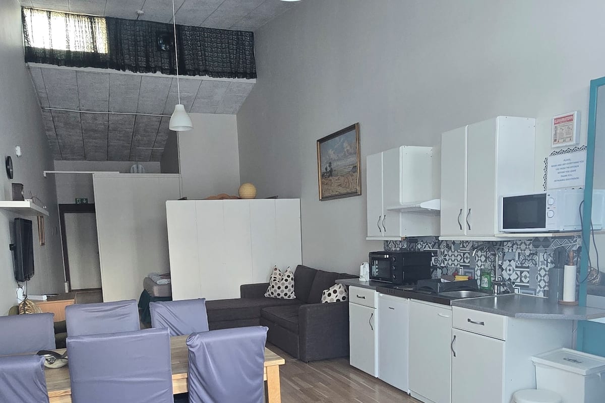 A compact kitchen with white cabinets, a microwave, and a sink. There is a dining area with a table and chairs.