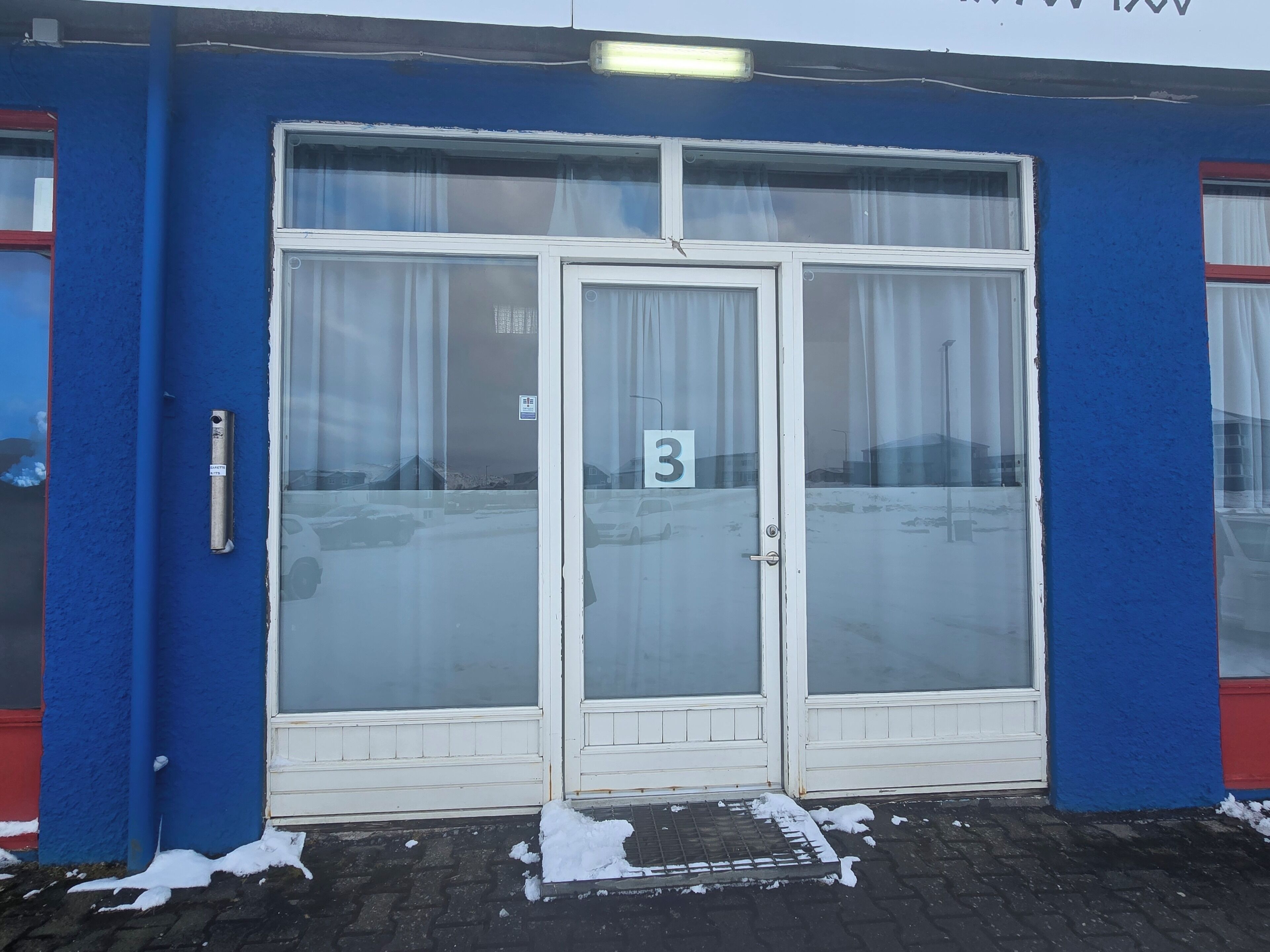A building with a blue exterior, a number '3' sign, and a glass door with a metal handle.