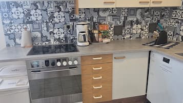 A compact kitchen with a gas stove, oven, and coffee maker. It features patterned tiles on the backsplash and a patterned rug on the floor.