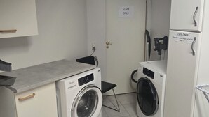 A compact laundry room with two front-loading washing machines, a small table, and a door marked "STAFF ONLY". - Reykjanes Guesthouse (Grindavik)