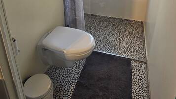 Ein Badezimmer mit Toilette, einem Händetrockner, einem Fenster und einem gefliesten Boden.