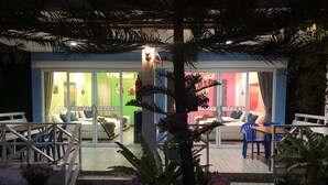 Ein Hotel mit einer Terrassenfläche, einem Esstisch und Stühlen. Im Vordergrund befinden sich zwei kleine Statuen.