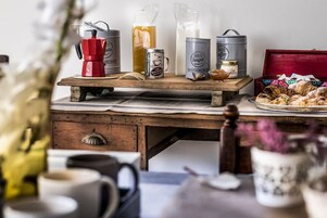 Ein Holztisch mit verschiedenen Kaffee- und Teebehältern, einer roten Kaffeekanne und Gebäck.