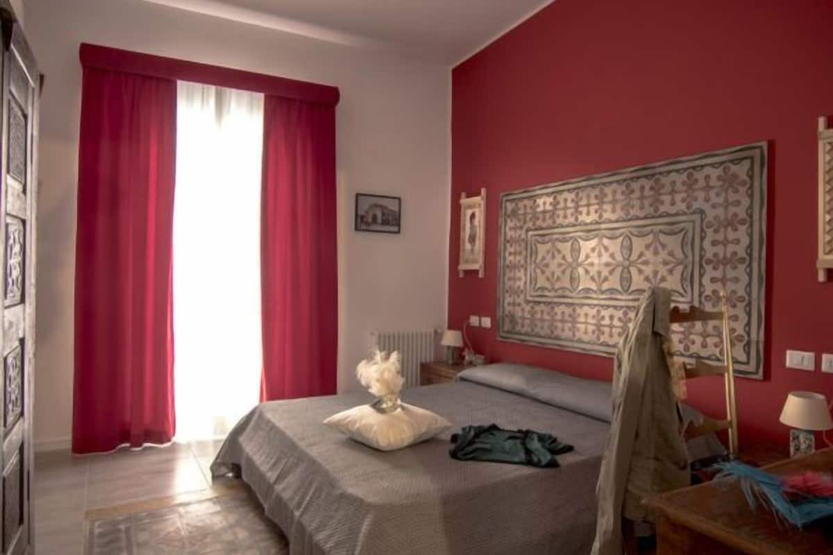 A bedroom with a bed, a red curtain, a patterned headboard, and a wooden dresser.