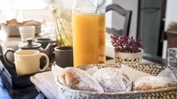 Desayuno con pasteles, un calentador de té, una jarra de jugo de naranja y un florero con flores.