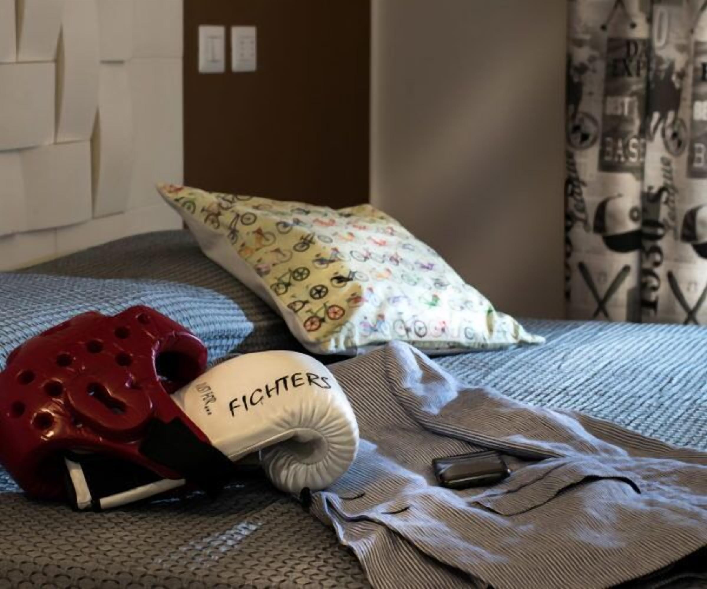 Una cama con una almohada estampada, un casco rojo, una almohada blanca con texto y una prenda doblada.