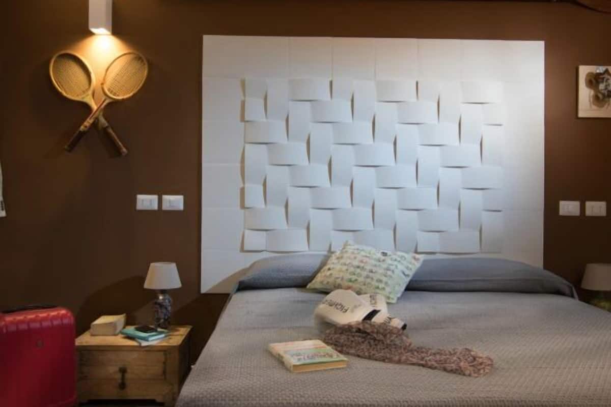 A bedroom with a modern headboard, a red suitcase, a lamp, and a book on the nightstand.