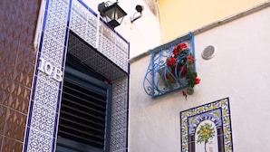 A building with a blue and white patterned door, a small window with a potted plant, and a decorative tile on the wall. - Mirabilia Arab House (Mazara del Vallo)