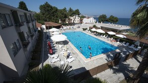 A swimming pool with lounge chairs and umbrellas, surrounded by buildings and a view of the sea. - Otel Diyojen (Sinop)