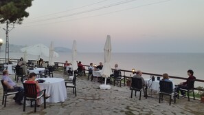 An outdoor dining area with tables and chairs, overlooking a body of water. - Otel Diyojen (Sinop)