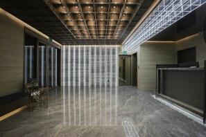 Un vestíbulo moderno con techo alto, una columna central y una mesa de recepción.