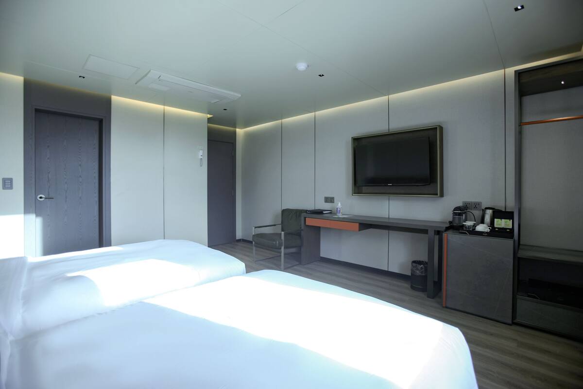 Een moderne hotelkamer met twee bedden, een bureau, een televisie en een kledingkast.