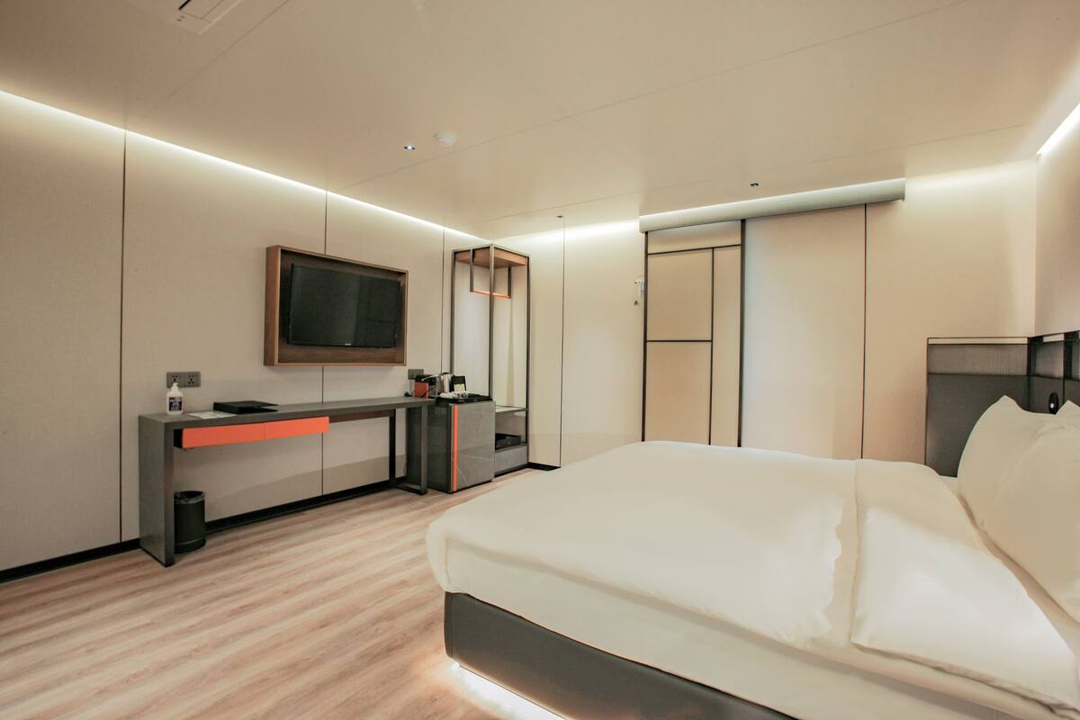 Een moderne hotelkamer met een bed, een bureau, een televisie en een kledingkast.