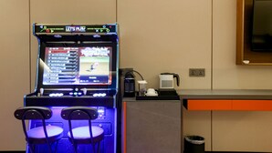 Une console de jeux avec deux fauteuils devant, une machine à café et un téléviseur fixé au mur.